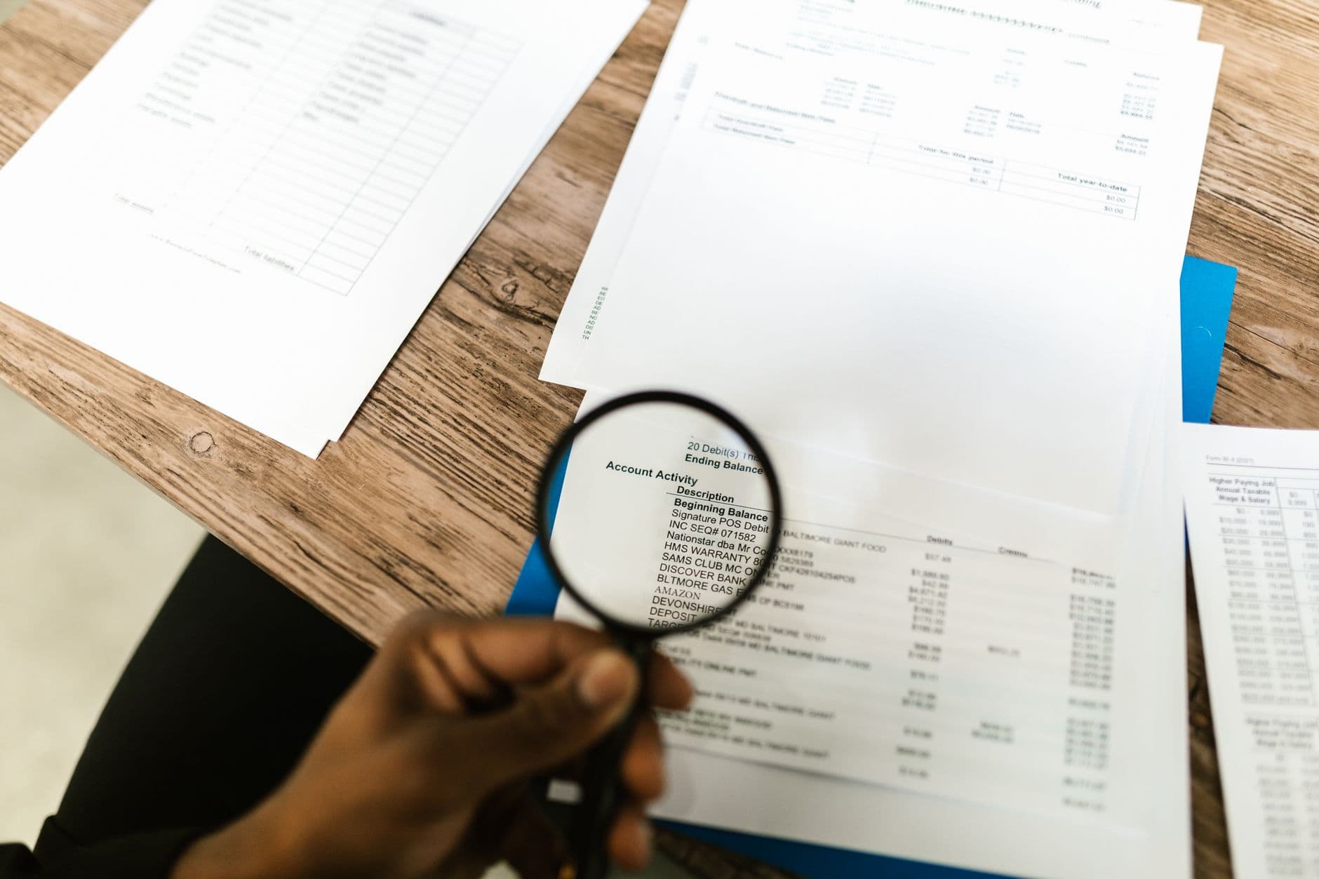 Close-up of hand using magnifying glass to review documents. Ideal for financial themes.